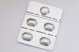 A blister pack of medication showing four oval-shaped tablets with text indicating Mifepristone and Misoprostol dosages on a light background.